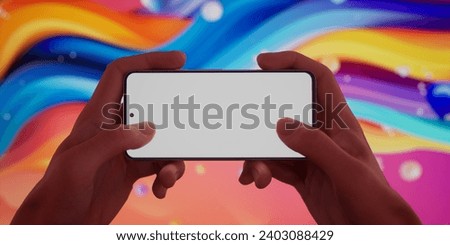 Caucasian man using a phone in two hands on bright vivid rainbow background, blank white screen smartphone mockup. Horizontal orientation. Playing games, watching video, streaming content