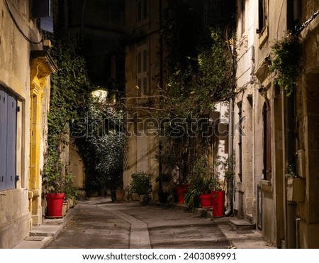 Narrow charming street in the old part of Arles, France, called La Roquette. Night picture, street lamps, chiaroscuro atmosphere. Royalty-Free Stock Photo #2403089991