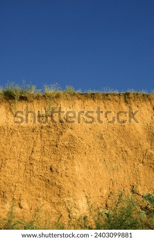 Clay cliffs on Bug estuary, chestnut soil layer. Change in lightness or color tone of object depending on environment called simultaneous color contrast - blue of sky is enhanced by break yellow-ochre Royalty-Free Stock Photo #2403099881