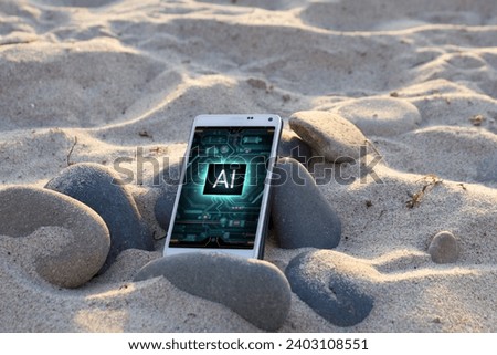 
A white smartphone with the bright blue socket AI on the display app open rests on a pile of smooth on a sandy beach. Sunlight glints off phone's screen. Artificial intelligence photo for header
