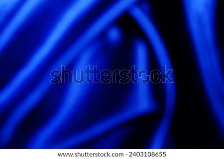 The surface is wavy, silk satin texture. Draped fabric on a blue background, luxurious and beautiful, with space for design, close-up, blur or blur.