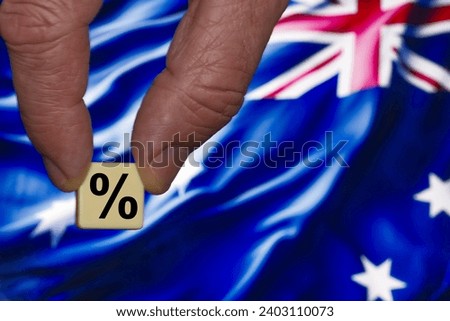 Fingers holding a single block with a black percent sign on the background of the Australia flag.