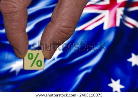 Fingers holding a single block with a green percent sign on the background of the Australia flag.