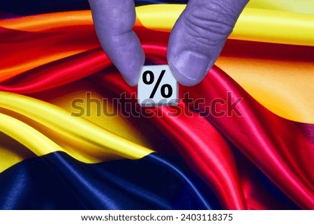 Fingers holding a single block with a black percent sign on the background of the German flag.