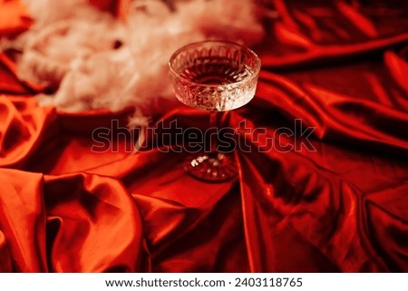 Extravagant glamour background with coupe glass of sparkly wine for love party at muffled light. Beautiful romantic burlesque place for st valentines holiday in red silk glossy sheets Royalty-Free Stock Photo #2403118765