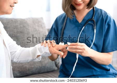 young asian female nurse measuring pulse with oximeter to a senior woman at home,selective focus at hands,concept of elderly people lifestyle,homecare,home health nursing  Royalty-Free Stock Photo #2403120693