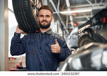 With brand new tire. Car repairman is in the garage with automobile. Royalty-Free Stock Photo #2403132387