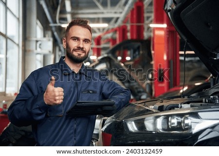 Using tablet. Car repairman is in the garage with automobile. Royalty-Free Stock Photo #2403132459