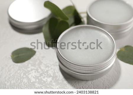 Lip balms and green leaves on white textured background, closeup Royalty-Free Stock Photo #2403138821