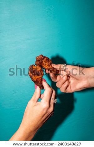 Vibrant Flash Photography: Female Hand Holding Flavorful American Tapas Chicken Wings with Dripping Sauce on a Bright Blue Background