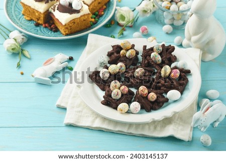 Easter chocolate nest cake with mini chocolate candy eggs with blossoming cherry or apple flowers on blue background table. Creative recipe for Easter table with holiday decorations. Top view. Royalty-Free Stock Photo #2403145137