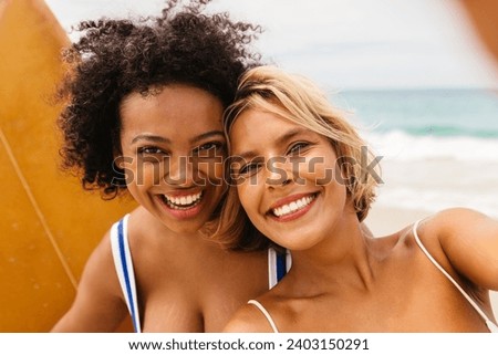 Happy female surfers preserve the joy of their fun beach moments through a lively selfie, capturing the essence of their adventurous spirit and the beauty of their surfing journey.
