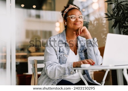 Young woman works remotely in a cozy coffee shop, using a laptop. She is a freelance content writer, focused and pensive as she works on her website writing project.