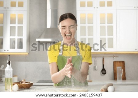 Funny woman clapping floury hands over messy table in kitchen Royalty-Free Stock Photo #2403159437