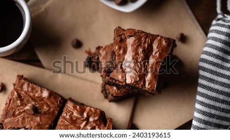 Chocolate chip brownies accompanied by coffee and chocolate chips, presented on a wooden board alongside a fork and knife, with baking paper enhancing