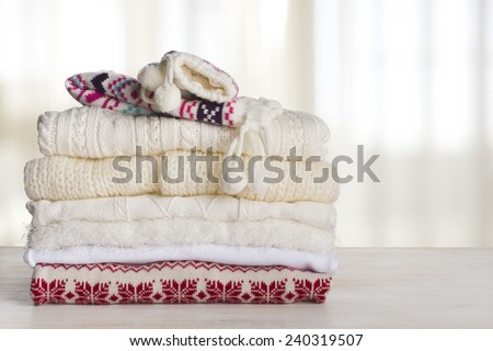 Pile of winter clothes on table over curtained window background