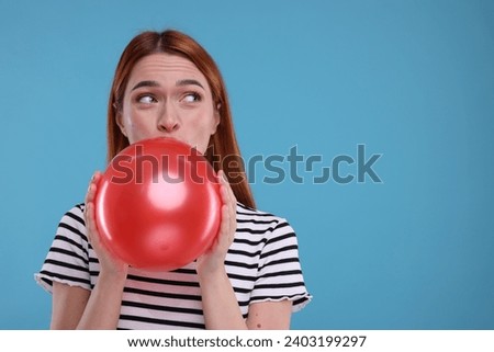 Woman inflating red balloon on light blue background, space for text