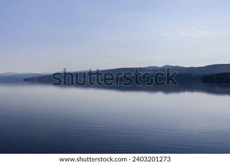 A tranquil scene at Snåsavatnet, Norway, with a lush, forested shoreline mirrored in the lake's still waters, highlighting the serene and unspoiled beauty of the Steinkjer region Royalty-Free Stock Photo #2403201273