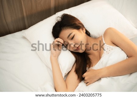 Asian woman sleeping in comfortable bed with silky linens in the morning. Women lying in bed and keeping eyes closed while covered with blanket. Content and peaceful, cheerful and comfortable.