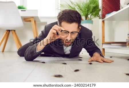 Shocked young business man in suit lying on white floor in his house or office, holding his glasses, and looking at lots of cockroaches crawling everywhere. Concept of roach infestation at home