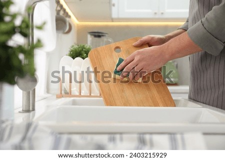 Man washing wooden cutting board at sink in kitchen, closeup