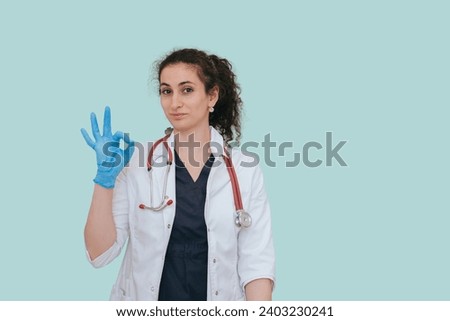 Brunette female doctor makes ok gesture looks at camera wearing medical clothes standing against transparent background. Satisfied nurse after successful day.