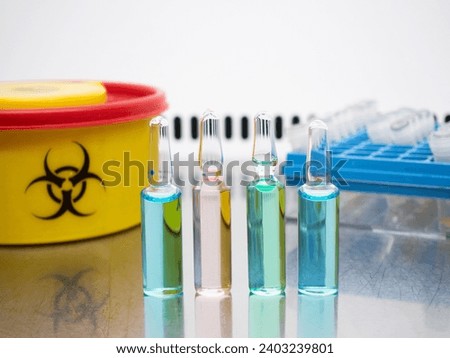 A set of ampoules with different colored liquids on a table in the laboratory. Ampoules next to a biohazard waste sign and test tubes in a box.