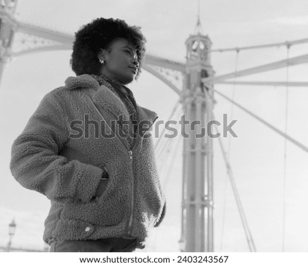Nostalgic black and white portrait of young black woman standing under bridge structure. It is cold morning day. Image made with analog medium format camera.