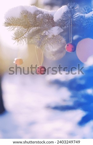 Red Christmas bell hangs on a snow-covered branch of a Christmas tree against a festive background of white snow and golden bokeh lights with copy space. New Year, greeting and holiday card, banner.