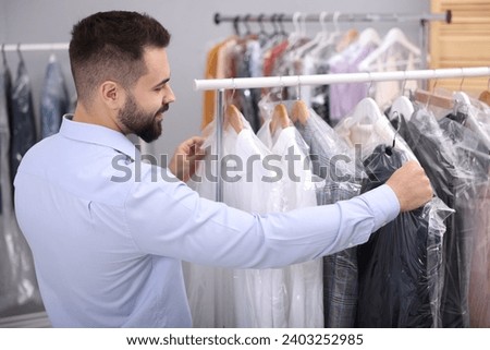 Dry-cleaning service. Worker choosing clothes from rack indoors Royalty-Free Stock Photo #2403252985