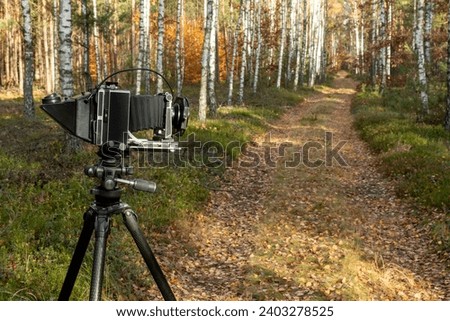 
Large format view camera on a tripod standing on a forest road with filter holder attached to the lens. Analog photography hobby.