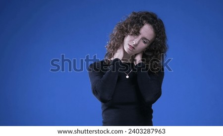 Stressed young woman rubbing neck trying to appease mental anguish while standing on blue background Royalty-Free Stock Photo #2403287963
