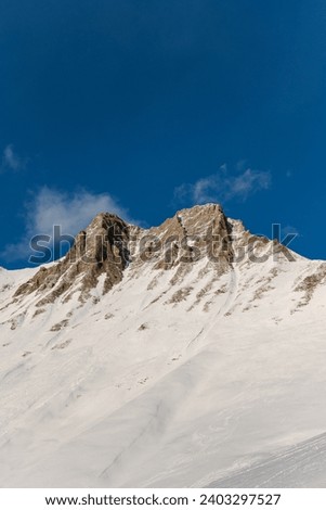 Snow-covered slope with a drift of white snow with a brown peak without snow against a blue sky