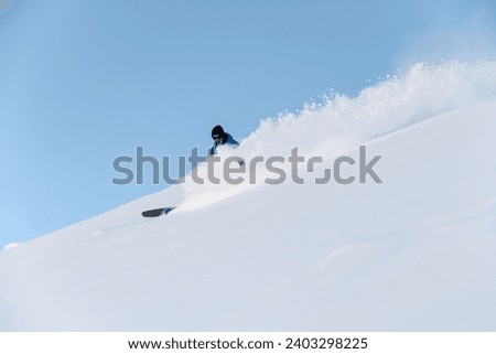 Male skier in a blue jacket goes down a snowy slope, so that he is almost invisible behind the powder snow Royalty-Free Stock Photo #2403298225