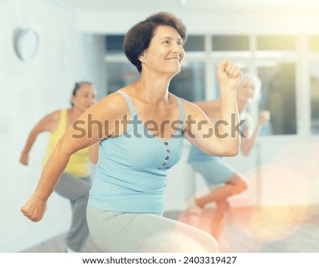 Cheery elderly woman engaged in dancing in fitness studio together with other attendees