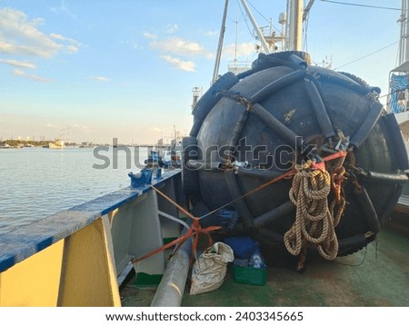 Black buoy floating lacated beside the ship, carrier, right-hand side of the ship. cover by chains, close to the loading, unloading channel. Used for mooring ships during in port and transport concept