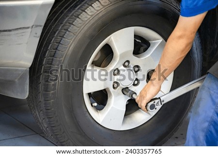 Auto mechanic using Torque wrench to inspection the wheel nuts for safety in travel in mechanics garage. Mechanic screwing or unscrewing changing car wheel by Socket wrench. Royalty-Free Stock Photo #2403357765