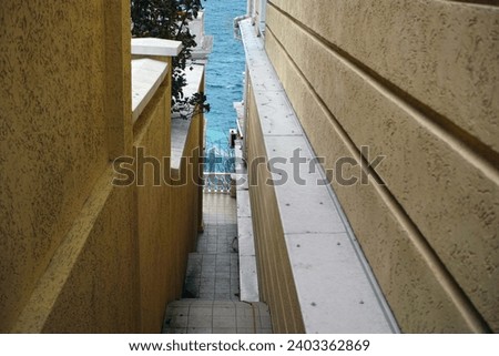 a narrow stairway leading downhill to the sea between two buildings  Royalty-Free Stock Photo #2403362869