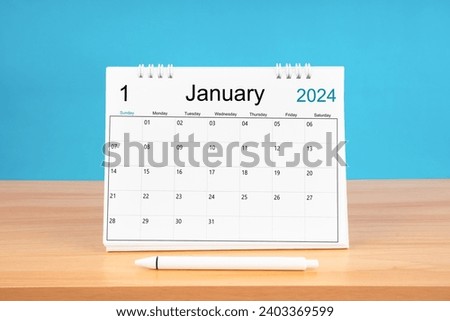 January monthly desk calendar for 2024 year and pen on wooden table with blue color background.