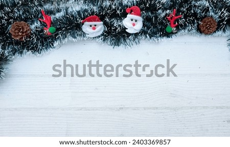Christmas decoration frame from decorated green fir branches of a Christmas tree and 
Cute cartoon Santa Claus,cones  decorative ornaments on  a white wooden table backdrop. Empty place fortext .  