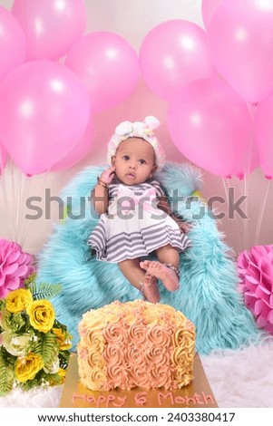 Little 6 months baby girl with pink balloons decoration and cake