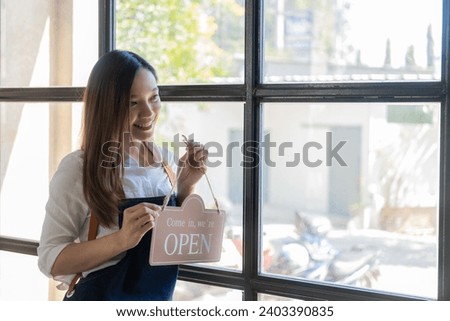 Happy young business owner standing holding open sign Happy Asian woman wearing an apron hanging a shop opening sign smile happily Proud in personal business