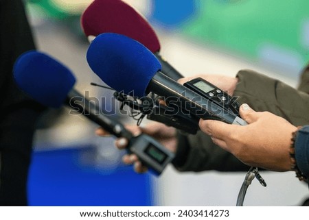 A poised group of journalists with microphones and cameras ready to delve into the heart of an event.   Royalty-Free Stock Photo #2403414273