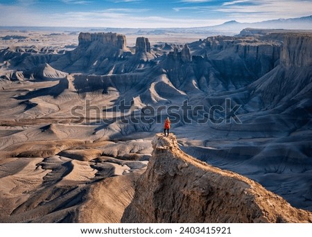 Woman in red jacket on cliff above colorful canyon. Moonscape overlook. Hanksville. Utah. USA Royalty-Free Stock Photo #2403415921