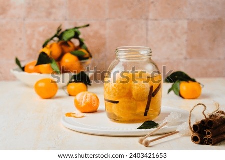 Whole tangerines in syrup with cinnamon sticks and vanilla in a glass jar on a light concrete background. Sweets, preserves, preparations. Tangerine recipes.