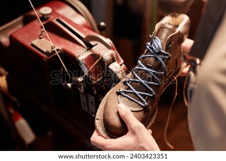 Workpiece of new brown leather boot in hands of young male shoemaker Royalty-Free Stock Photo #2403423351