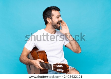 Young man with guitar over isolated blue background shouting with mouth wide open to the lateral