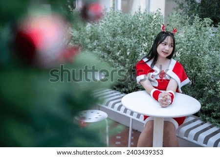 Portrait Cute Smiling asian girl in red santa with looking to the camera near Christmas greeting picture parcel decoration on Christmas tree background Decoration During Christmas and New Year.