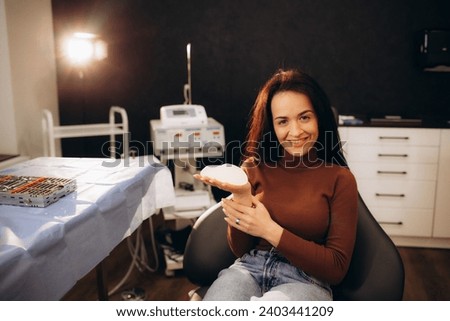Close-up of happy smiling young woman holding gel implant. Cheerful medical worker looking surprised. Clinic appointment. Modern medicine and body correction concept