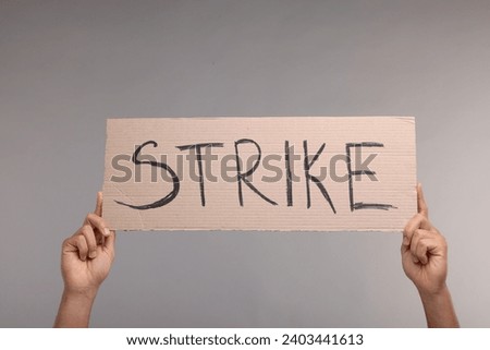 Man holding cardboard banner with word Strike on grey background, closeup